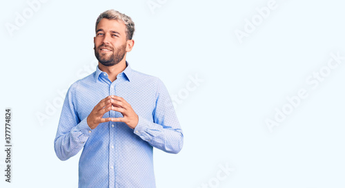 Young handsome blond man wearing elegant shirt hands together and fingers crossed smiling relaxed and cheerful. success and optimistic