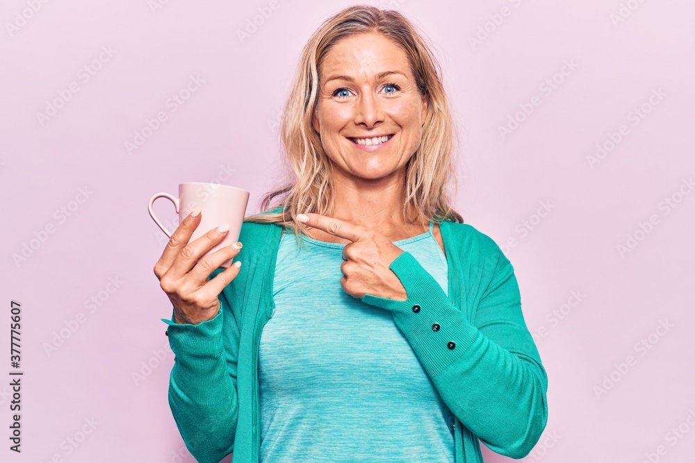 Middle age caucasian blonde woman drinking a cup of coffee smiling happy pointing with hand and finger Middle age caucasian blonde woman drinking a cup of coffee smiling happy pointing with hand and finger
