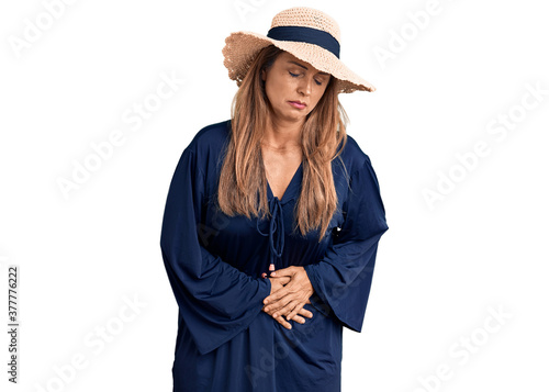 Middle age hispanic woman wearing summer hat with hand on stomach because indigestion, painful illness feeling unwell. ache concept.