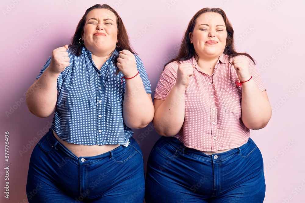 Young plus size twins wearing casual clothes excited for success with arms raised and eyes closed celebrating victory smiling. winner concept. Young plus size twins wearing casual clothes excited for success with arms raised and eyes closed celebrating victory smiling. winner concept.