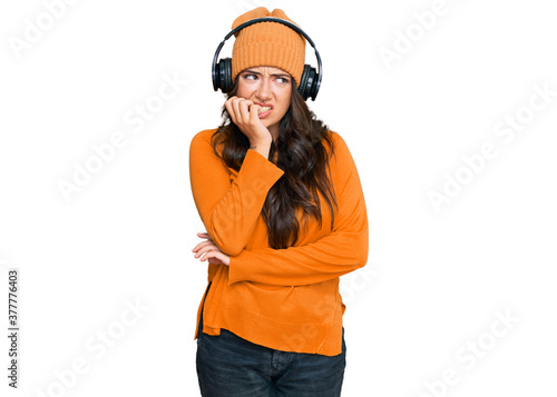 Beautiful brunette young woman listening to music using headphones looking stressed and nervous with hands on mouth biting nails. anxiety problem. © Krakenimages.com
