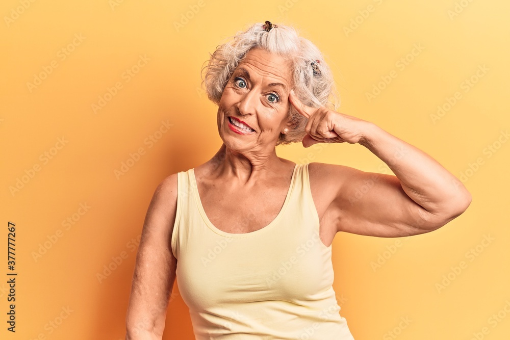 Senior grey-haired woman wearing casual clothes smiling pointing to head with one finger, great idea or thought, good memory Senior grey-haired woman wearing casual clothes smiling pointing to head with one finger, great idea or thought, good memory