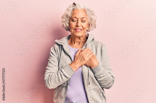 Senior grey-haired woman wearing casual sporty clothes smiling with hands on chest with closed eyes and grateful gesture on face. health concept.