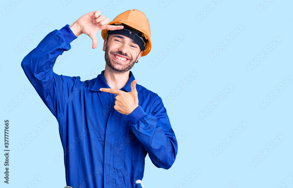 Young hispanic man wearing worker uniform smiling making frame with hands and fingers with happy face. creativity and photography concept.