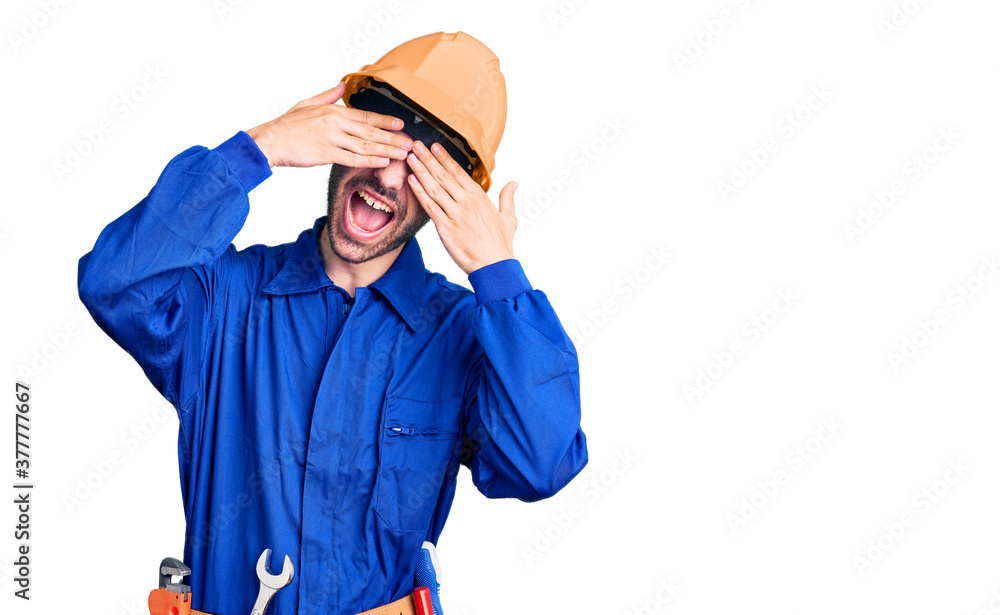 Young hispanic man wearing worker uniform covering eyes with hands smiling cheerful and funny. blind concept. Young hispanic man wearing worker uniform covering eyes with hands smiling cheerful and funny. blind concept.