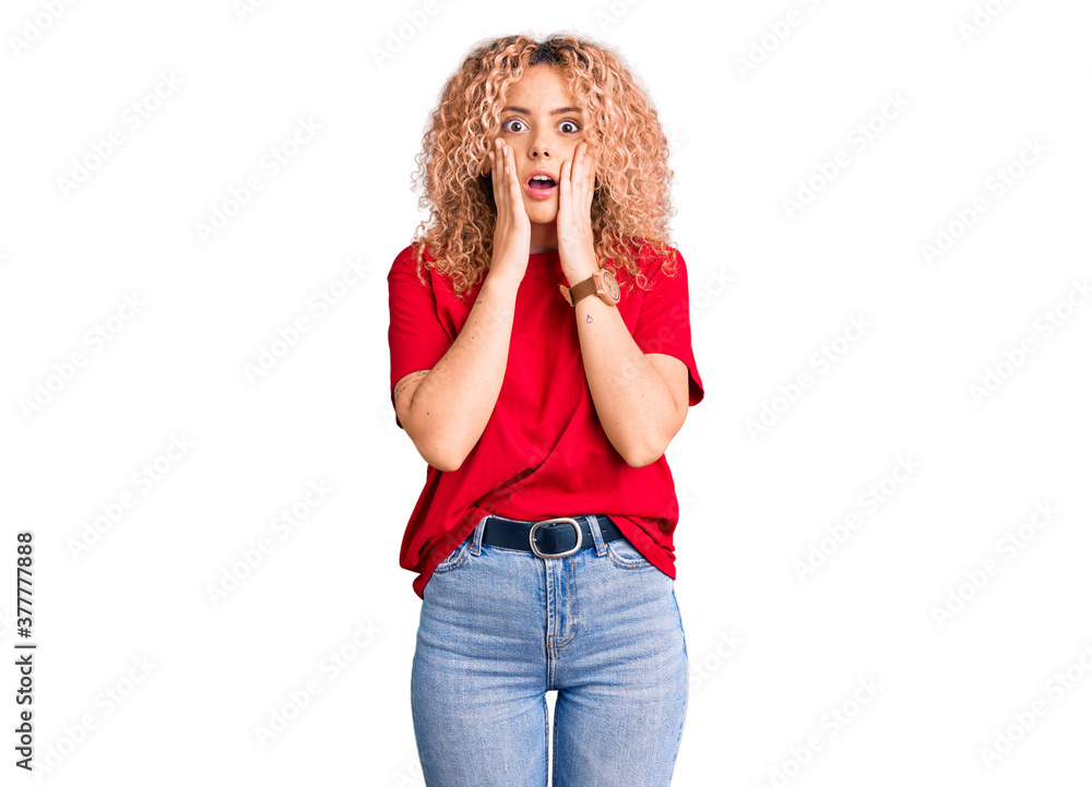 Young blonde woman with curly hair wearing casual red tshirt afraid and shocked, surprise and amazed expression with hands on face Young blonde woman with curly hair wearing casual red tshirt afraid and shocked, surprise and amazed expression with hands on face