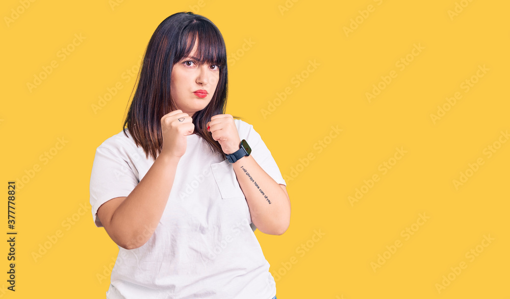 Young plus size woman wearing casual clothes ready to fight with fist defense gesture, angry and upset face, afraid of problem Young plus size woman wearing casual clothes ready to fight with fist defense gesture, angry and upset face, afraid of problem