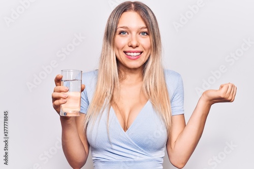Young beautiful blonde girl drinking glass of water screaming proud, celebrating victory and success very excited with raised arm © Krakenimages.com