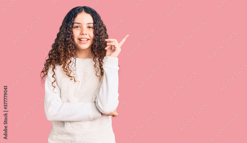 Beautiful kid girl with curly hair wearing casual clothes with a big smile on face, pointing with hand and finger to the side looking at the camera. Beautiful kid girl with curly hair wearing casual clothes with a big smile on face, pointing with hand and finger to the side looking at the camera.