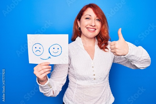 Redhead coach woman asking for depression holding paper with emotion change message smiling happy and positive, thumb up doing excellent and approval sign