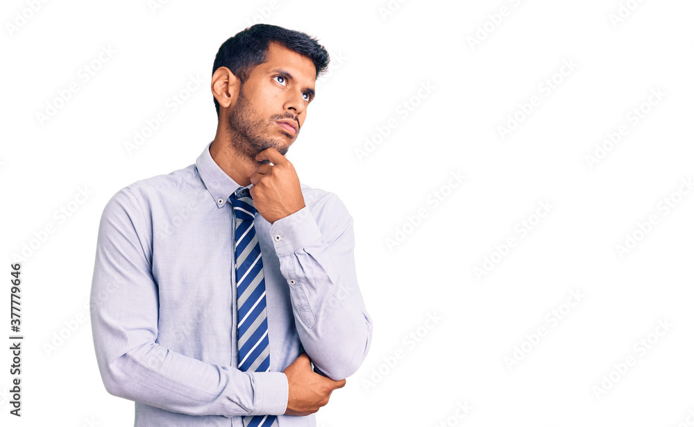 Young latin man wearing business clothes serious face thinking about question with hand on chin, thoughtful about confusing idea Young latin man wearing business clothes serious face thinking about question with hand on chin, thoughtful about confusing idea