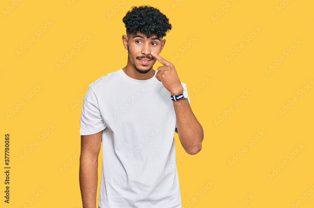 Young arab man wearing casual white t shirt pointing with hand finger to face and nose, smiling cheerful. beauty concept Young arab man wearing casual white t shirt pointing with hand finger to face and nose, smiling cheerful. beauty concept
