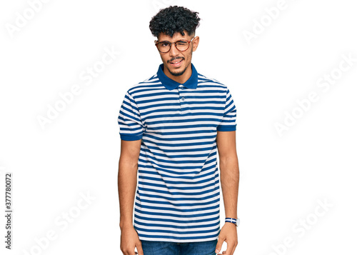 Young arab man wearing casual clothes and glasses winking looking at the camera with sexy expression, cheerful and happy face.