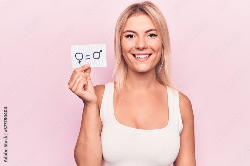 Young blonde woman asking for sex discrimination holding paper with gender equality message looking positive and happy standing and smiling with a confident smile showing teeth Young blonde woman asking for sex discrimination holding paper with gender equality message looking positive and happy standing and smiling with a confident smile showing teeth