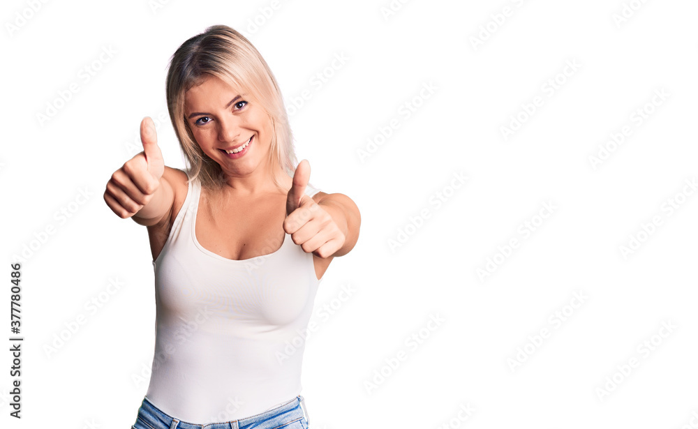 Young beautiful blonde woman wearing casual sleeveless t-shirt approving doing positive gesture with hand, thumbs up smiling and happy for success. winner gesture. Young beautiful blonde woman wearing casual sleeveless t-shirt approving doing positive gesture with hand, thumbs up smiling and happy for success. winner gesture.