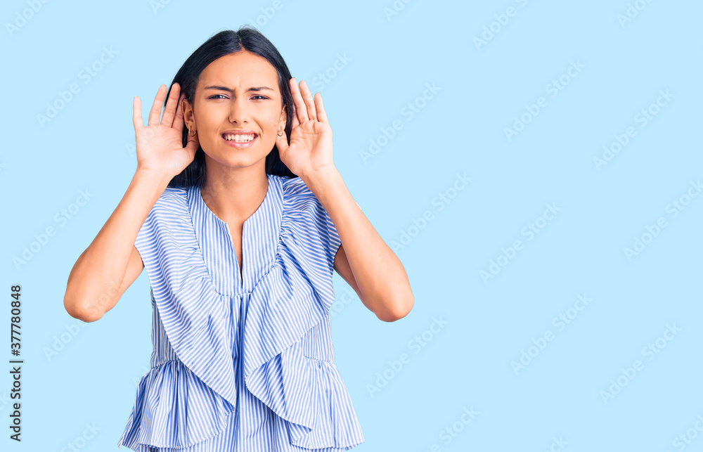 Young beautiful latin girl wearing casual clothes trying to hear both hands on ear gesture, curious for gossip. hearing problem, deaf Young beautiful latin girl wearing casual clothes trying to hear both hands on ear gesture, curious for gossip. hearing problem, deaf