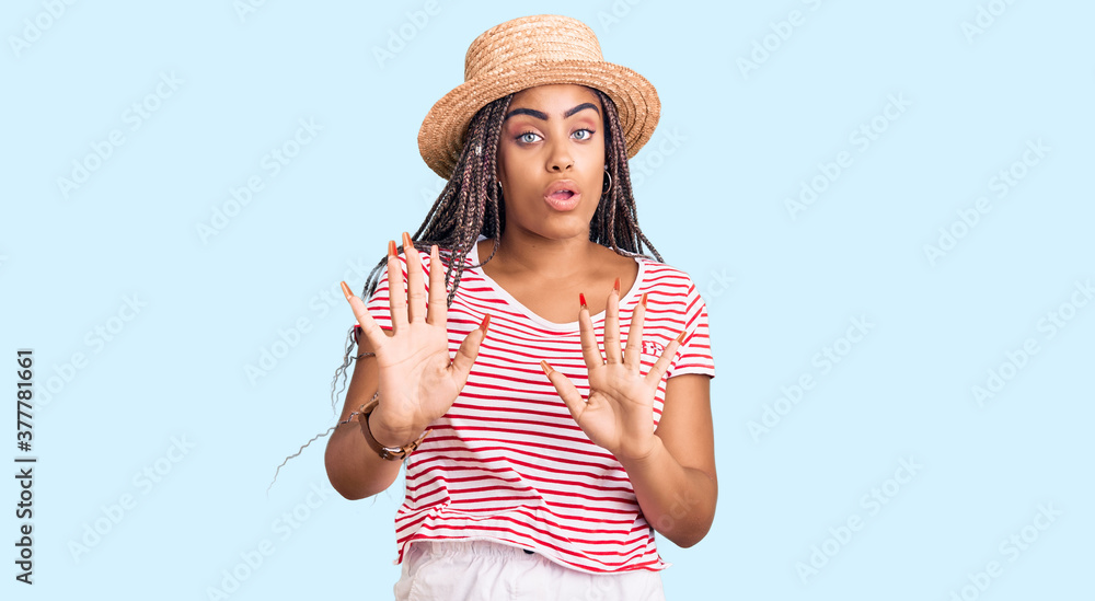Young african american woman with braids wearing summer hat moving away hands palms showing refusal and denial with afraid and disgusting expression. stop and forbidden.
