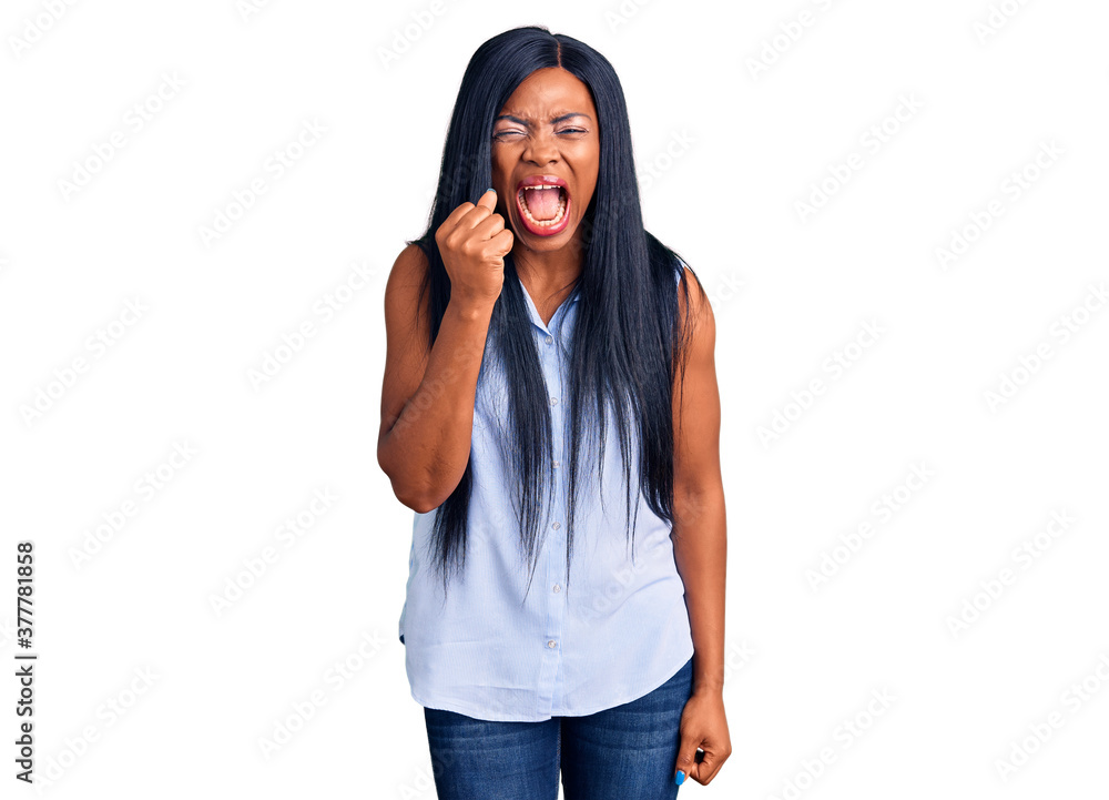 Young african american woman wearing casual clothes angry and mad raising fist frustrated and furious while shouting with anger. rage and aggressive concept. Young african american woman wearing casual clothes angry and mad raising fist frustrated and furious while shouting with anger. rage and aggressive concept.