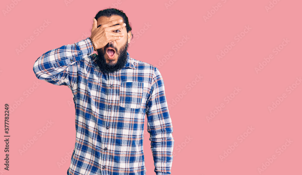 Fototapeta premium Young arab man wearing casual clothes peeking in shock covering face and eyes with hand, looking through fingers with embarrassed expression.