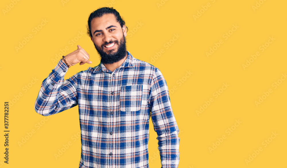 Young arab man wearing casual clothes smiling doing phone gesture with hand and fingers like talking on the telephone. communicating concepts. Young arab man wearing casual clothes smiling doing phone gesture with hand and fingers like talking on the telephone. communicating concepts.