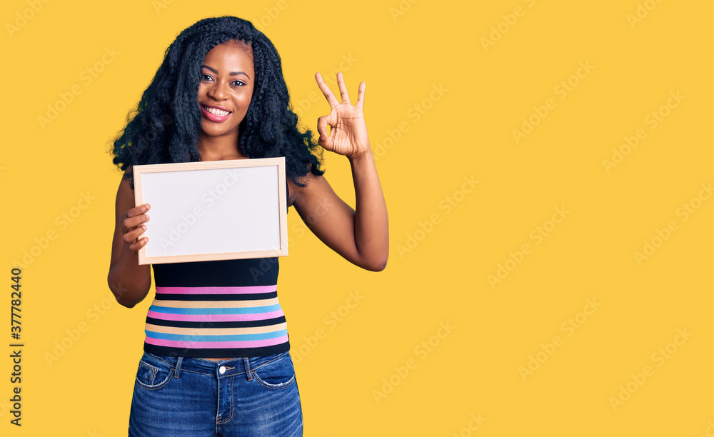 Beautiful african american woman holding blank empty banner doing ok sign with fingers, smiling friendly gesturing excellent symbol Beautiful african american woman holding blank empty banner doing ok sign with fingers, smiling friendly gesturing excellent symbol