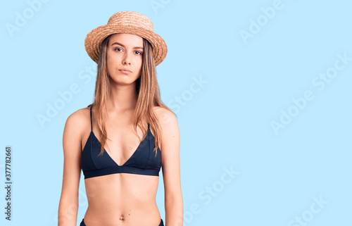 Young beautiful girl wearing bikini and hat relaxed with serious expression on face. simple and natural looking at the camera.