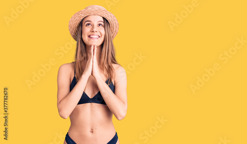 Young beautiful girl wearing bikini and hat begging and praying with hands together with hope expression on face very emotional and worried. begging.