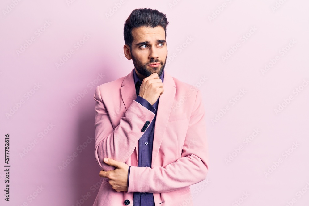 Young handsome man with beard wearing elegant jacket with hand on chin thinking about question, pensive expression. smiling with thoughtful face. doubt concept. Young handsome man with beard wearing elegant jacket with hand on chin thinking about question, pensive expression. smiling with thoughtful face. doubt concept.