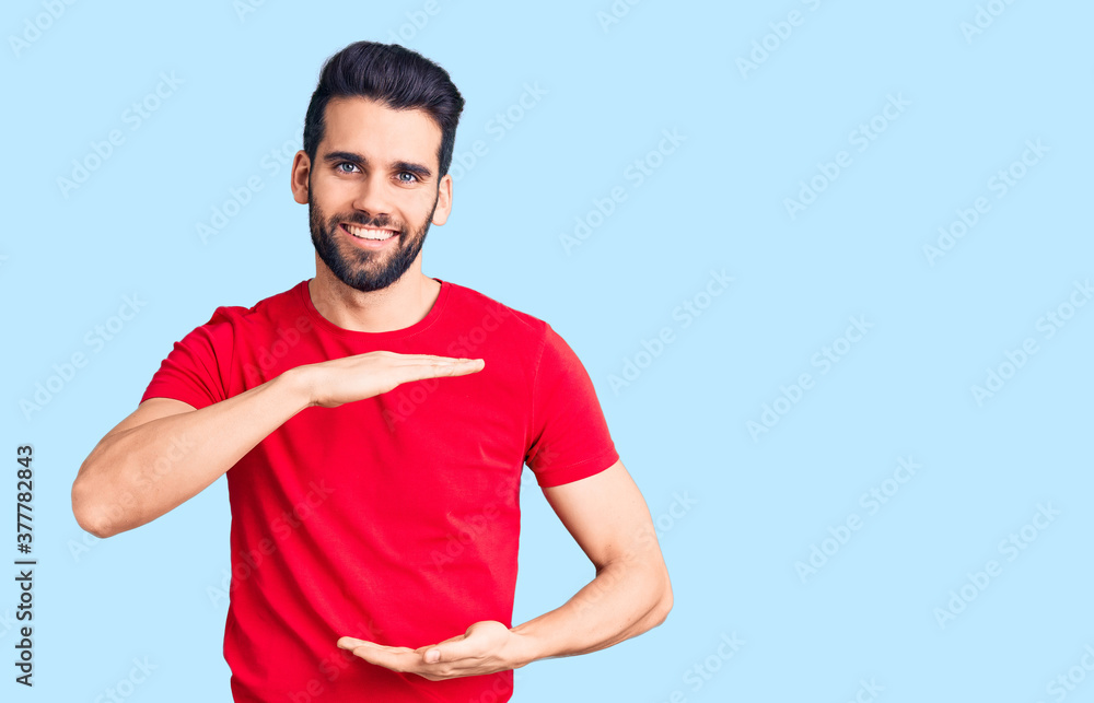 Young handsome man with beard wearing casual t-shirt gesturing with hands showing big and large size sign, measure symbol. smiling looking at the camera. measuring concept. Young handsome man with beard wearing casual t-shirt gesturing with hands showing big and large size sign, measure symbol. smiling looking at the camera. measuring concept.