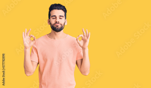 Young handsome man with beard wearing casual t-shirt relax and smiling with eyes closed doing meditation gesture with fingers. yoga concept. © Krakenimages.com