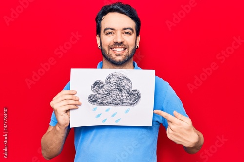 Young hispanic man holding rain draw smiling happy pointing with hand and finger © Krakenimages.com