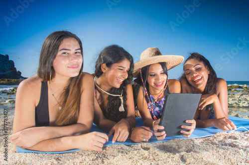 Multi ethnic group girls friends using social media in digital tablet at caribbean beach in Los Roques Venezuela