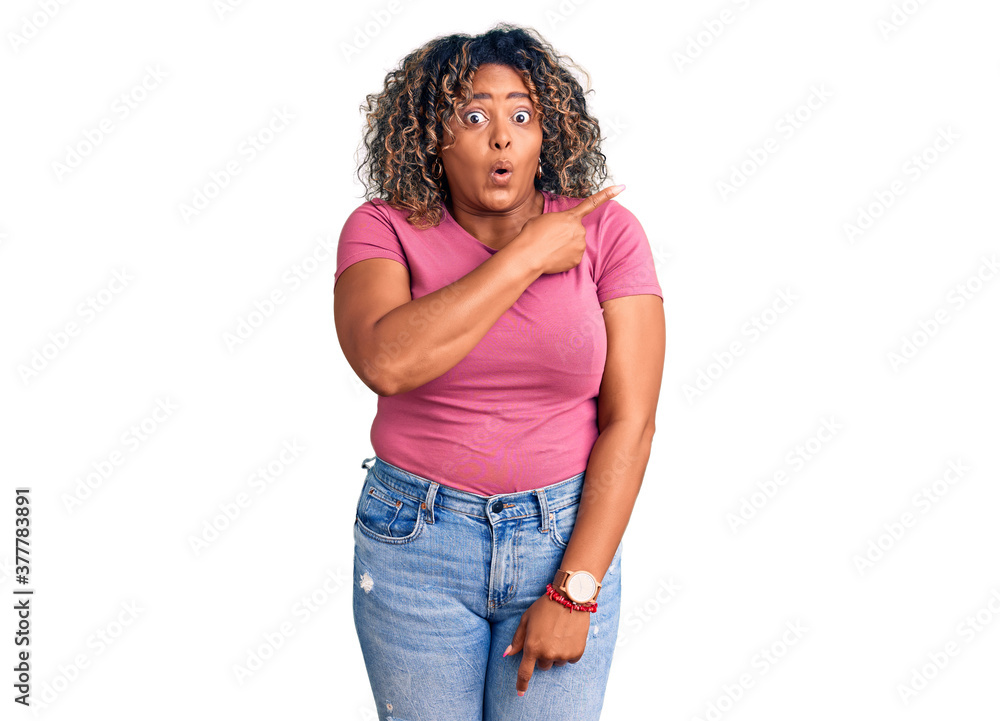 Young african american plus size woman wearing casual clothes surprised pointing with finger to the side, open mouth amazed expression. Young african american plus size woman wearing casual clothes surprised pointing with finger to the side, open mouth amazed expression.