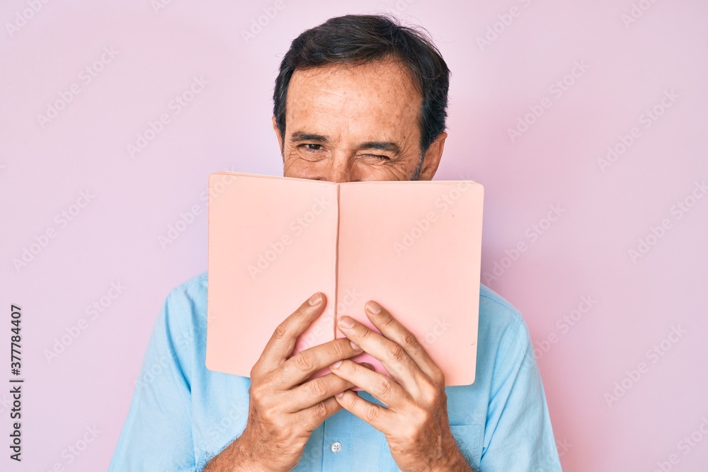 Middle age hispanic man reading book winking looking at the camera with sexy expression, cheerful and happy face. Middle age hispanic man reading book winking looking at the camera with sexy expression, cheerful and happy face.