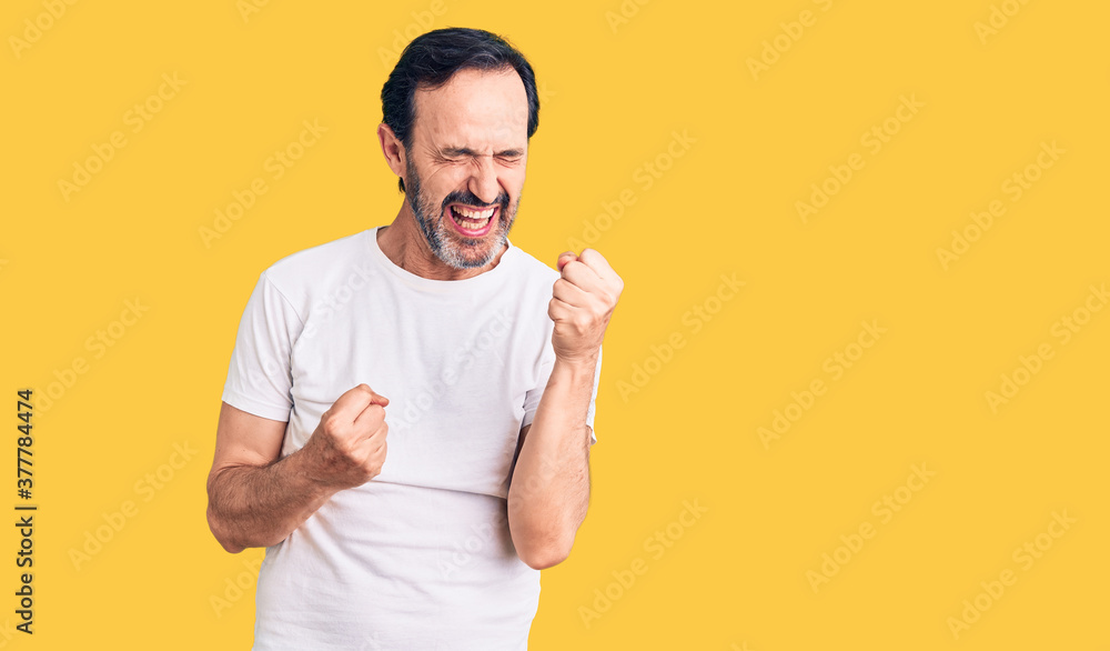 Middle age handsome man wearing casual t-shirt celebrating surprised and amazed for success with arms raised and eyes closed. winner concept. Middle age handsome man wearing casual t-shirt celebrating surprised and amazed for success with arms raised and eyes closed. winner concept.