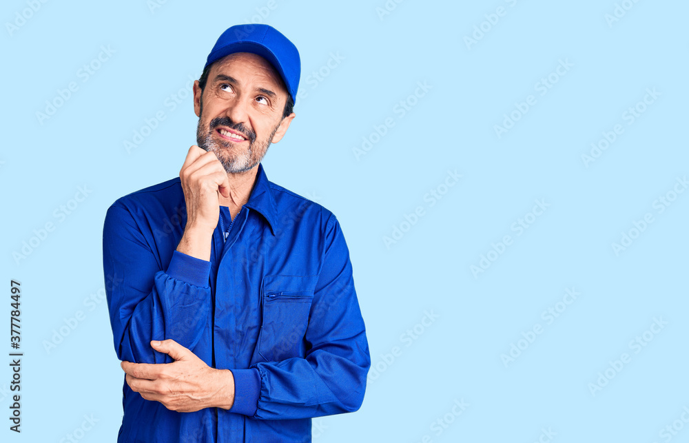 Middle age handsome man wearing mechanic uniform with hand on chin thinking about question, pensive expression. smiling and thoughtful face. doubt concept. Middle age handsome man wearing mechanic uniform with hand on chin thinking about question, pensive expression. smiling and thoughtful face. doubt concept.