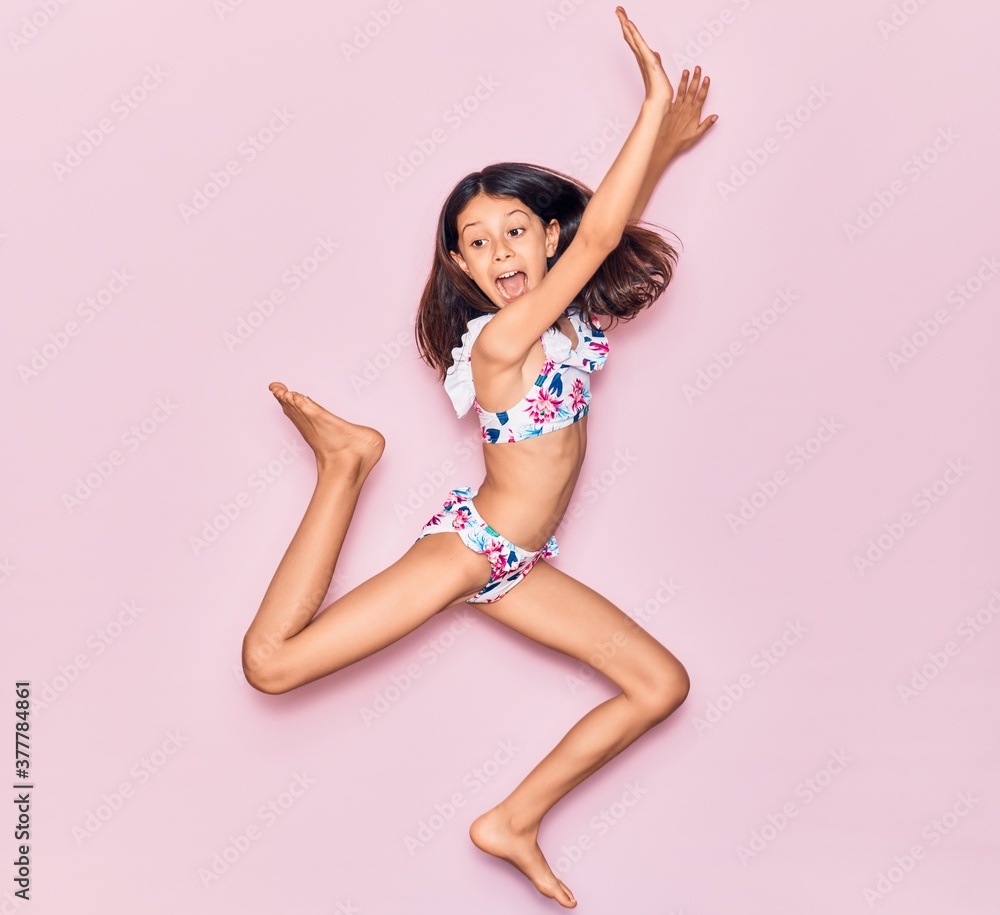 Adorable hispanic child girl on vacation wearing bikini surprised with open  mouth. Jumping over isolated pink background Stock Photo | Adobe Stock