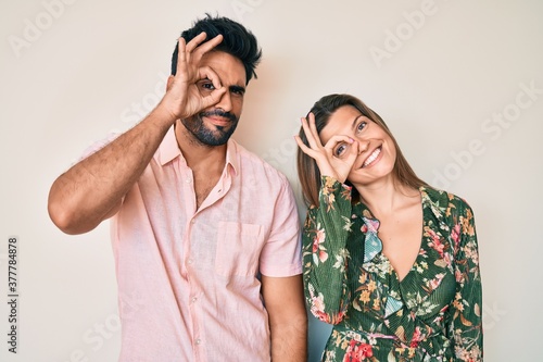 Beautiful young couple of boyfriend and girlfriend together doing ok gesture with hand smiling, eye looking through fingers with happy face.