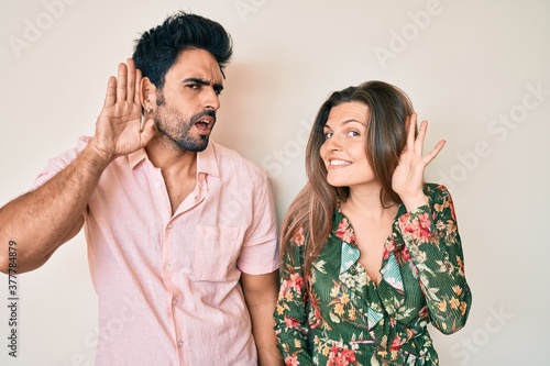 Beautiful young couple of boyfriend and girlfriend together smiling with hand over ear listening an hearing to rumor or gossip. deafness concept.