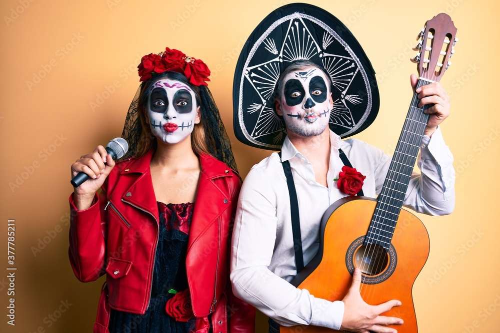 Couple wearing day of the dead costume playing classical guitar using microphone puffing cheeks with funny face. mouth inflated with air, catching air.