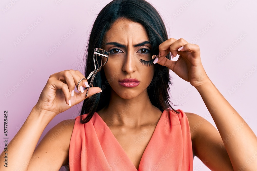 Beautiful hispanic woman holding eyelash curler and fake lashes skeptic and nervous, frowning upset because of problem. negative person.