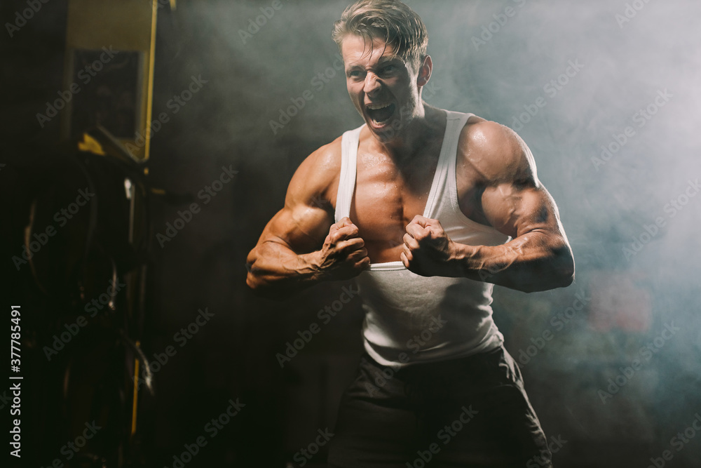 Powerful sexy muscular body model tearing shirt. muscular man showing muscles sweaty and furious in gym. Hot and handsome man tearing shirt. Fitness motivation background