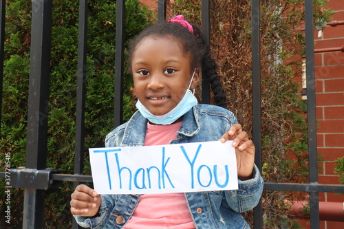 Child holding Thank You Sign outdoors with surgical mask pulled down