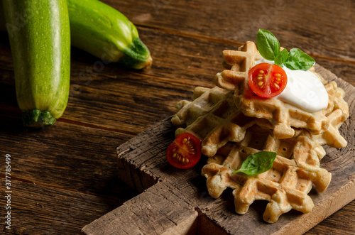 vegetarian zucchini waffles with herbs on a plate with fresh tomatoes, basil and sour cream on a wooden background.