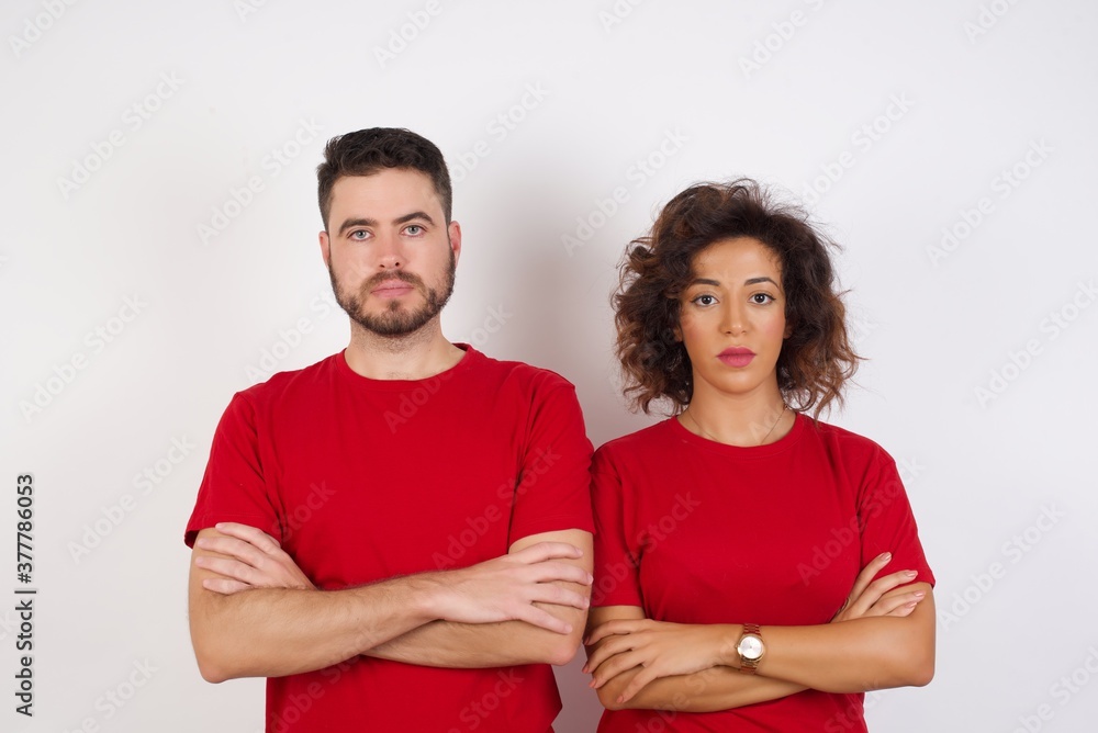 Young beautiful couple wearing red t-shirt on white background serious face with crossed arms looking at the camera. Positive person. Young beautiful couple wearing red t-shirt on white background serious face with crossed arms looking at the camera. Positive person.