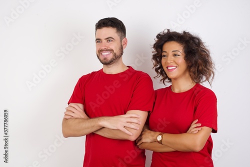 Young beautiful couple wearing red t-shirt on white background crossing arms looking aside having a nice conversation