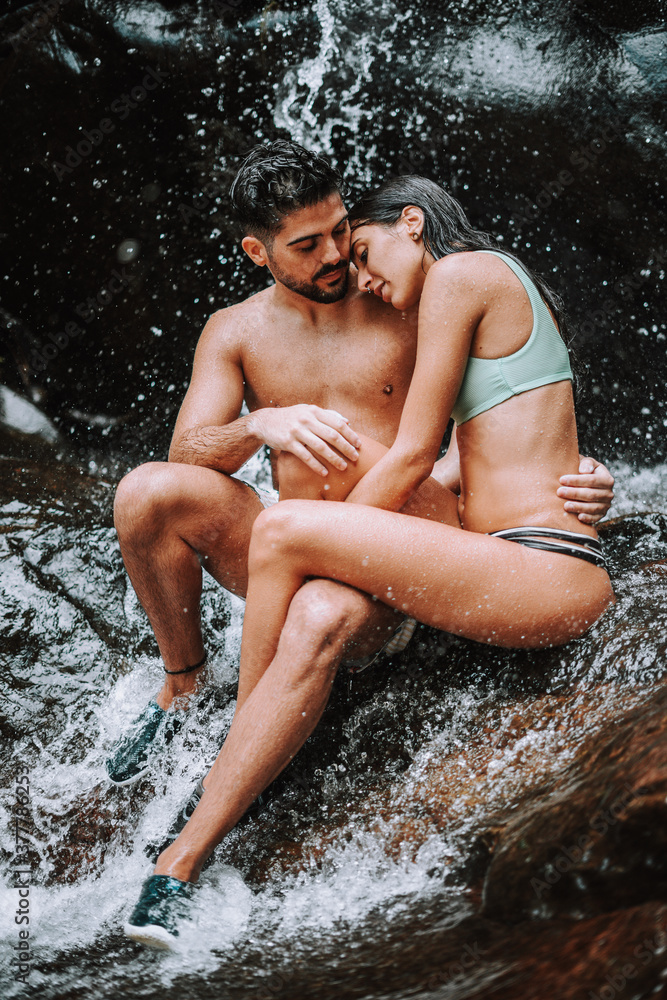 Obraz premium Pareja en un lago bajo una cascada en plena naturaleza disfrutando de una ruta en su viaje de vacaciones