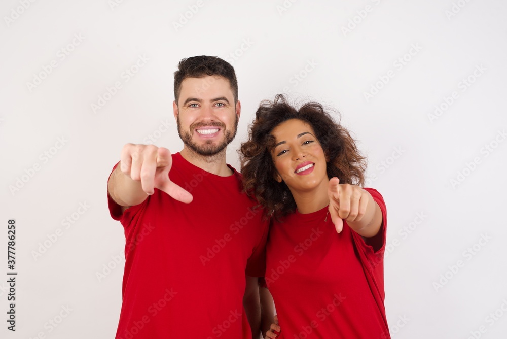 Obraz premium Young beautiful couple wearing red t-shirt on white background pointing at camera with a satisfied, confident, friendly smile, choosing you