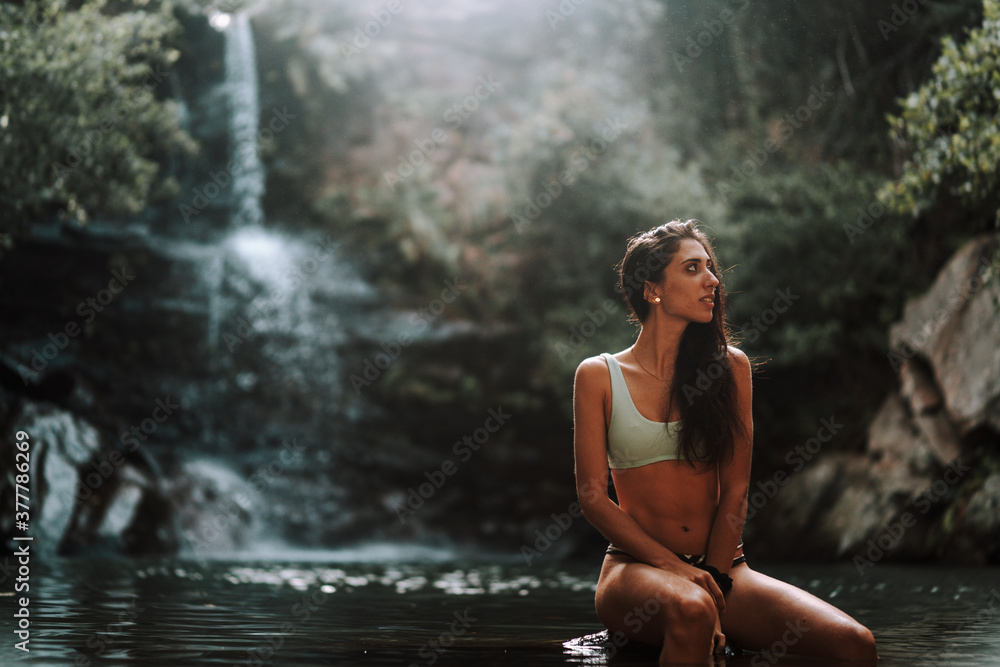 Chica joven atractiva en lago posando sobre una piedra