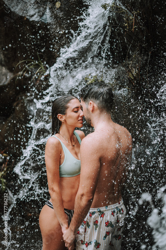 Pareja en un lago bajo una cascada en plena naturaleza disfrutando de una ruta en su viaje de vacaciones